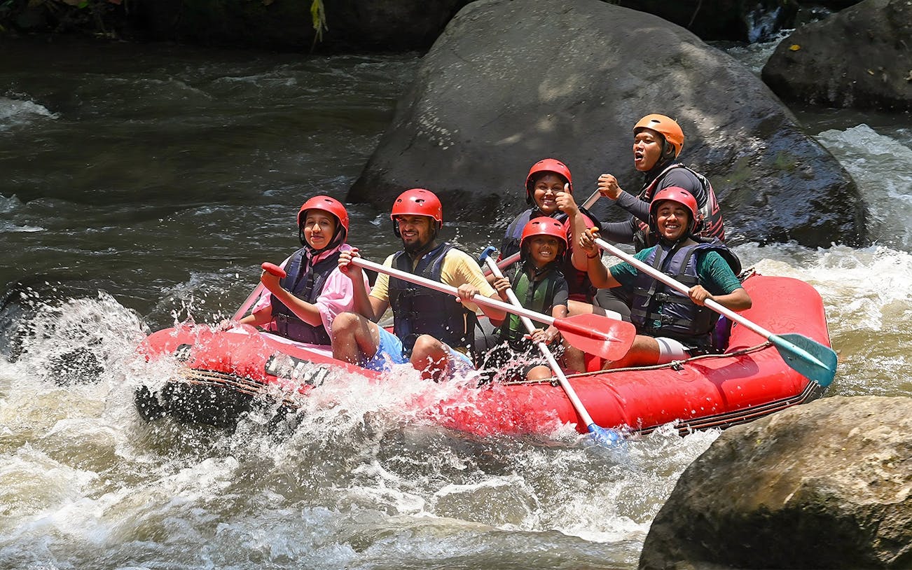 Group rafting on Ayung River in Ubud, navigating rapids in a red inflatable raft.
