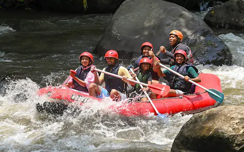 Group rafting on Ayung River in Ubud, navigating rapids in a red inflatable raft.