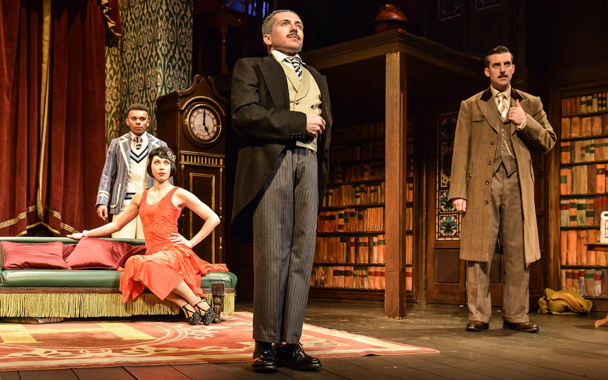 Actors performing a scene from "The Play That Goes Wrong" in a vintage library setting.