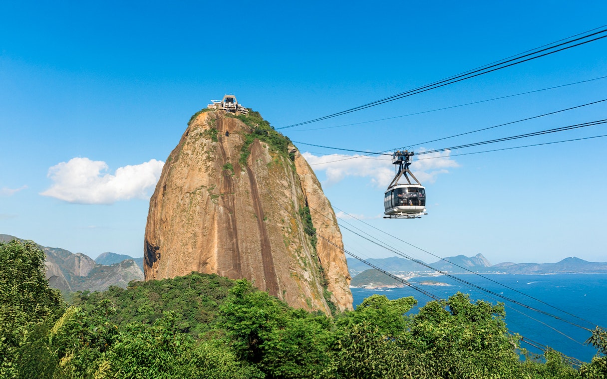 Cable car ascending Sugar Loaf Mountain over lush rainforest in Rio de Janeiro, Brazil.