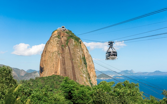 Cable car ascending Sugar Loaf Mountain over lush rainforest in Rio de Janeiro, Brazil.