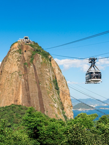 Cable car ascending Sugar Loaf Mountain over lush rainforest in Rio de Janeiro, Brazil.