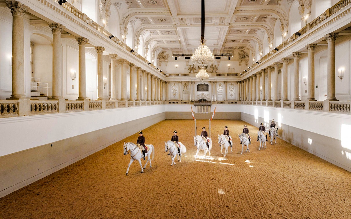 Spanish Riding School performance in Vienna arena with riders on white horses.