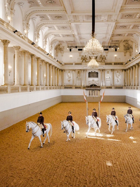 Spanish Riding School performance in Vienna arena with riders on white horses.