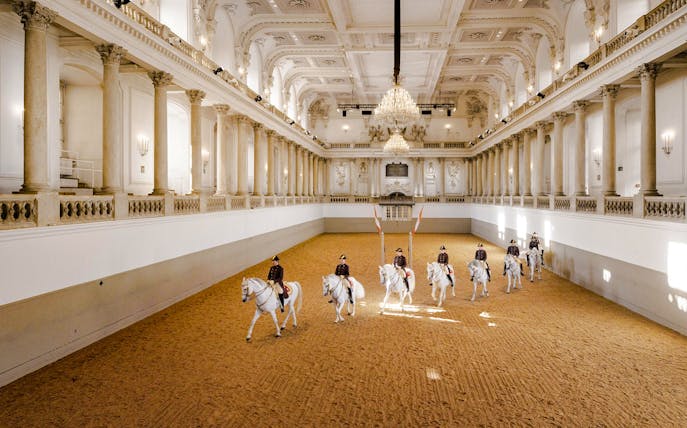 Spanish Riding School performance in Vienna arena with riders on white horses.