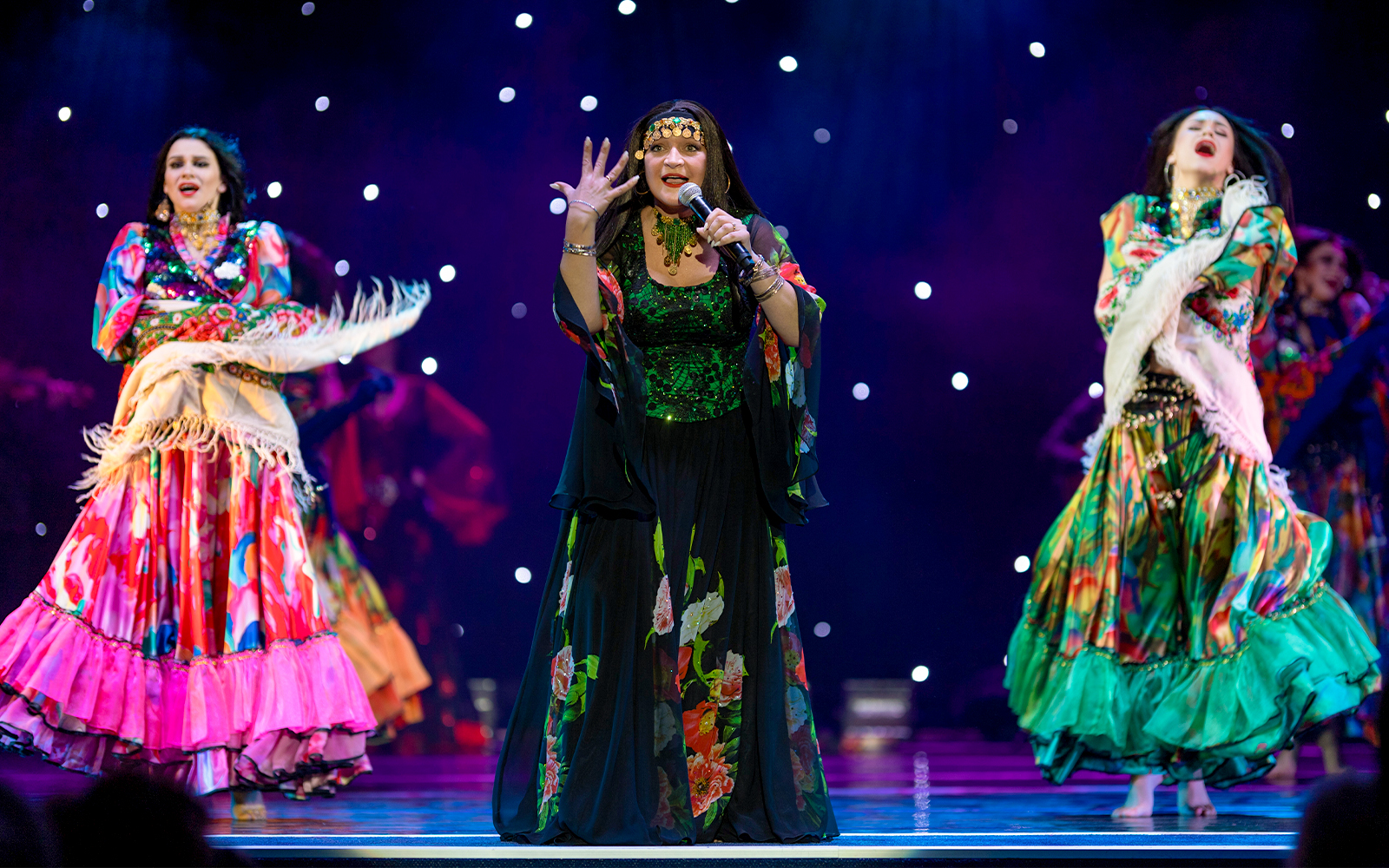 Flamenco dancers in colorful dresses performing on stage with a starry backdrop.