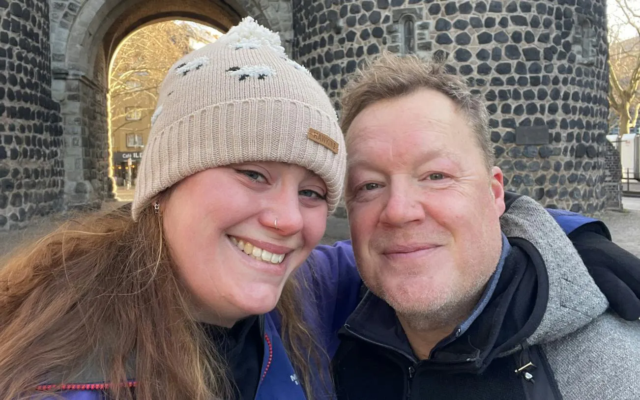 Two people smiling in front of a historic stone archway in Cologne.