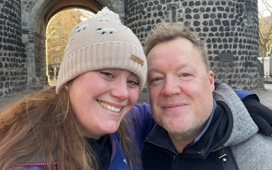 Two people smiling in front of a historic stone archway in Cologne.