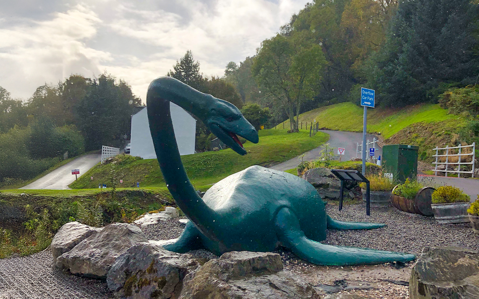 Loch Ness monster statue near a road and greenery in Scotland.