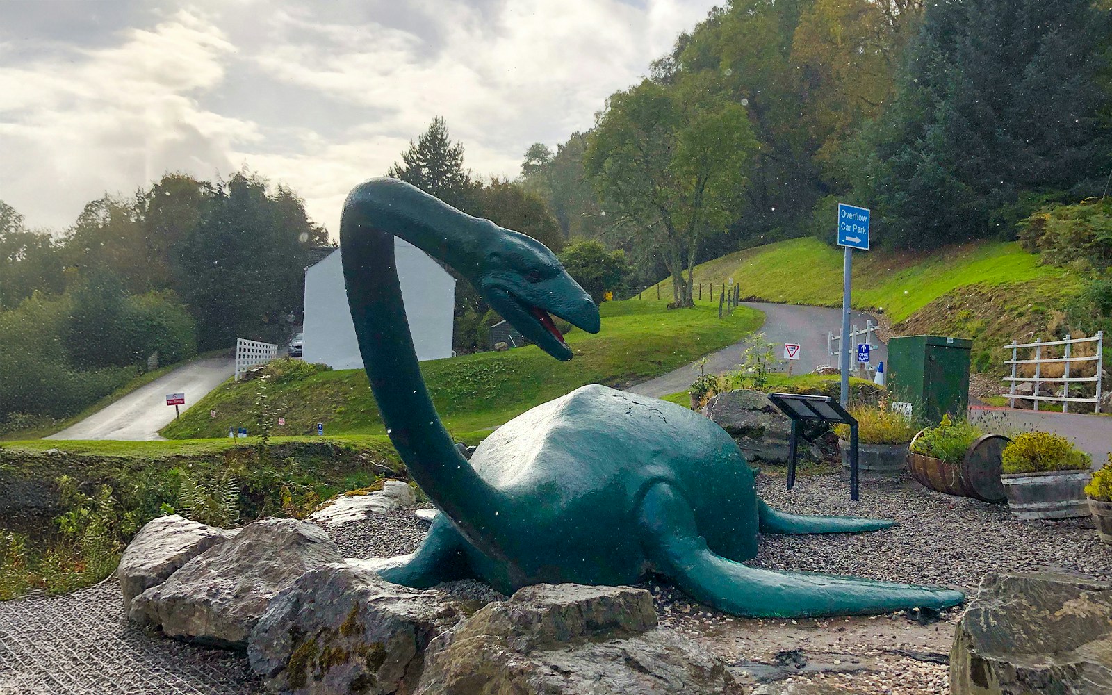 Loch Ness monster statue near a road and greenery in Scotland.