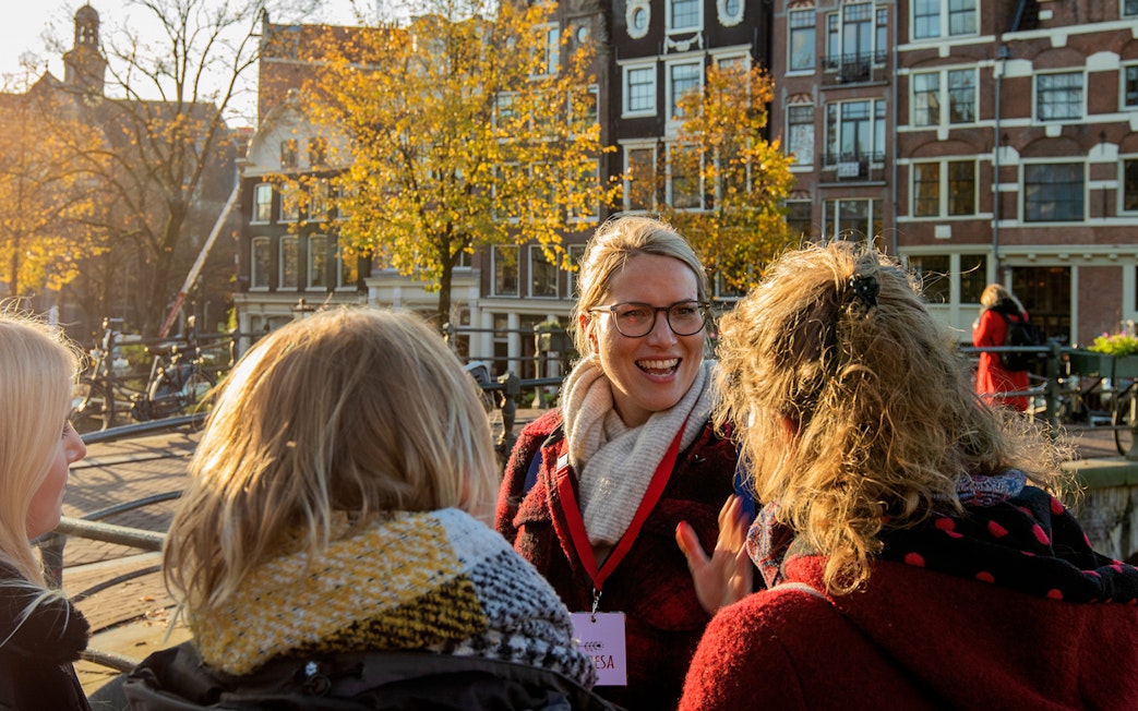 Tour guide leading a group in Amsterdam with historic canal houses in the background.