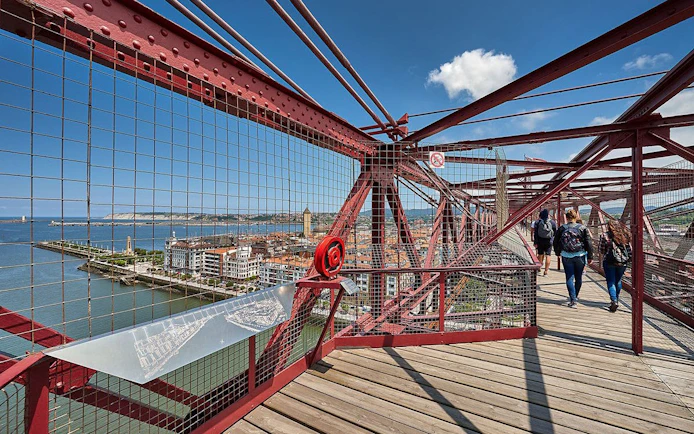Visitors walking on Biscay Bridge with city and river views in Portugalete, Spain.