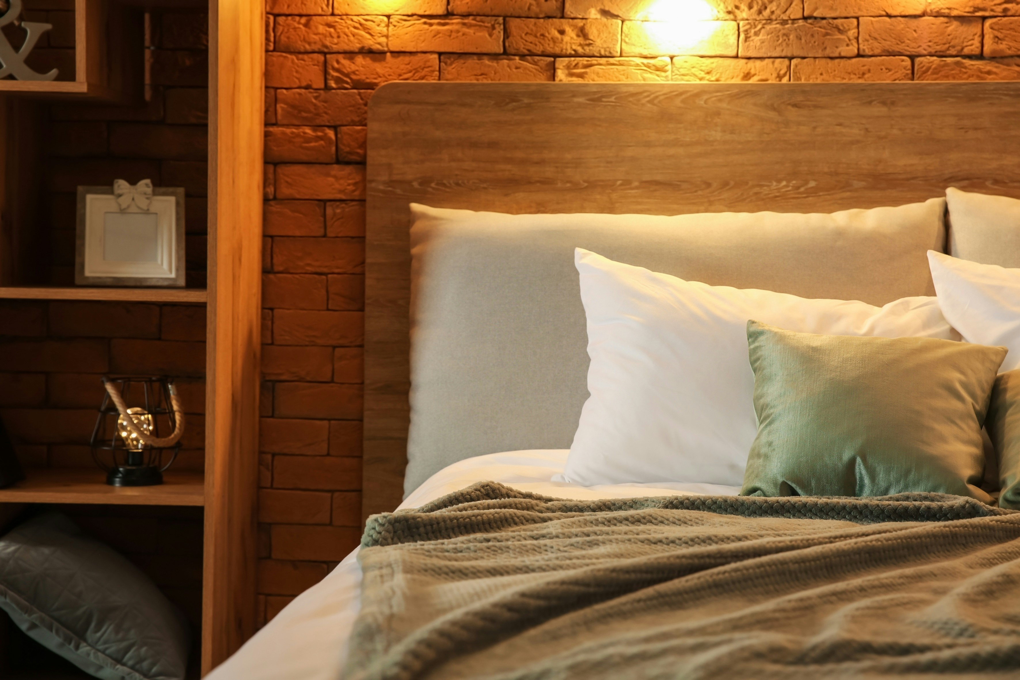 Cozy hotel room bed with pillows and a soft blanket against a brick wall.