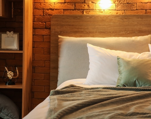 Cozy hotel room bed with pillows and a soft blanket against a brick wall.