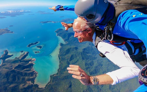 Tandem skydiving over Airlie Beach coastline, Queensland, with vibrant ocean and lush landscape below.