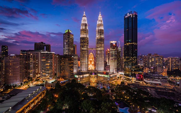 Petronas Twin Towers illuminated at dusk in Kuala Lumpur cityscape.