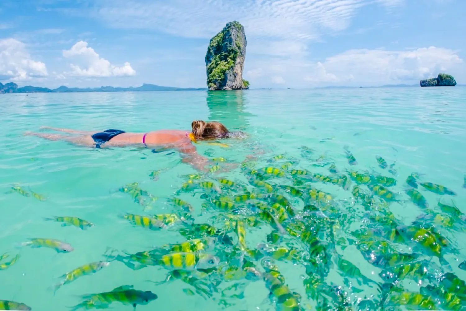 Snorkeler observing fish near limestone rock in Krabi's clear waters.