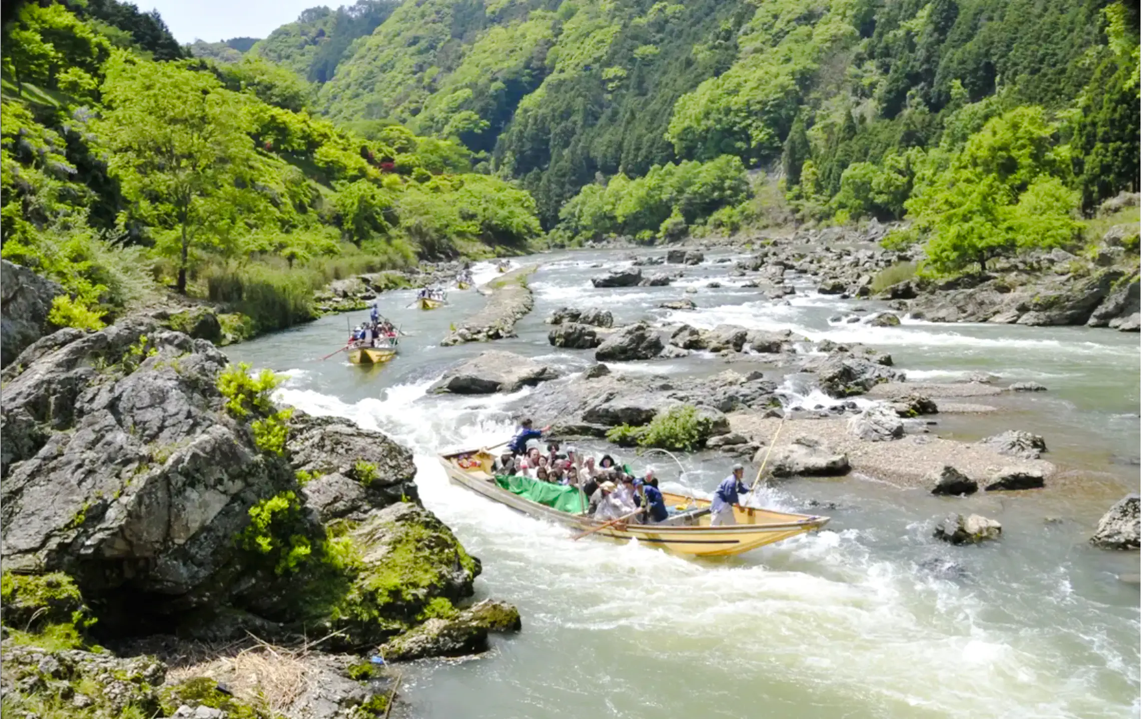 Boat tour on Hozugawa River with lush greenery and rocky landscape, Kyoto.