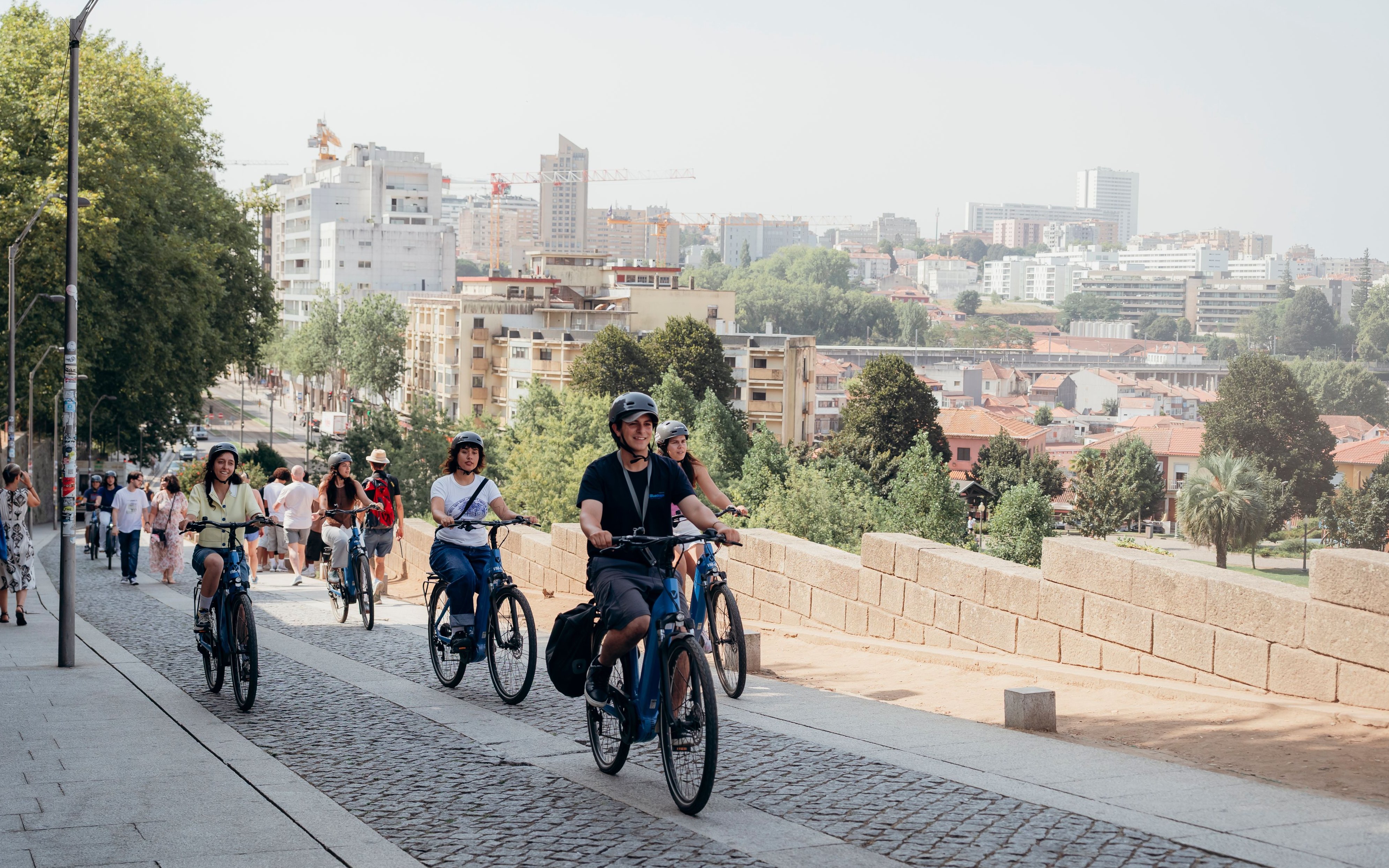 Tourists riding electric bikes with a guide in Porto, cityscape in the background.