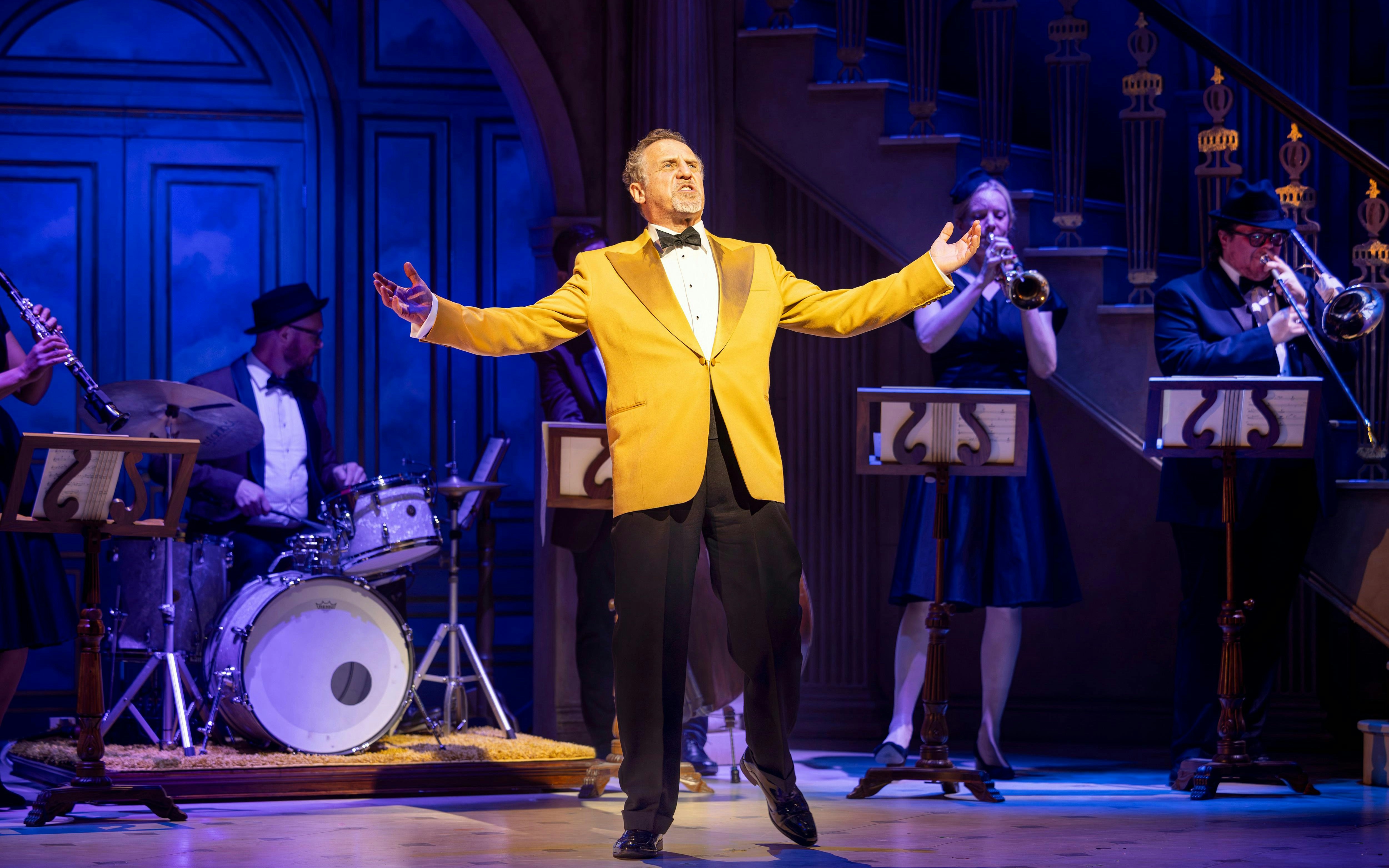 Stage performance of High Society in West End with a singer in a yellow jacket and live band.