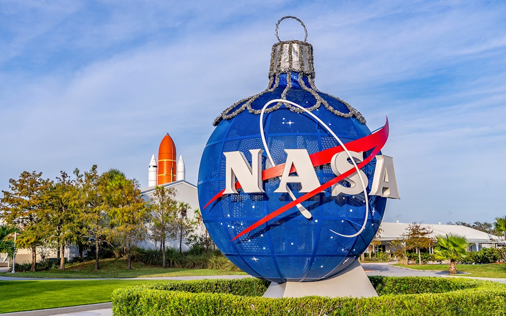 NASA globe sculpture at Kennedy Space Center with space shuttle in background.