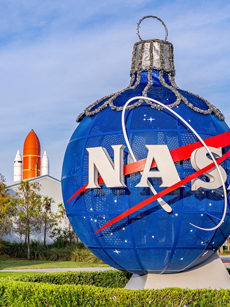 NASA globe sculpture at Kennedy Space Center with space shuttle in background.