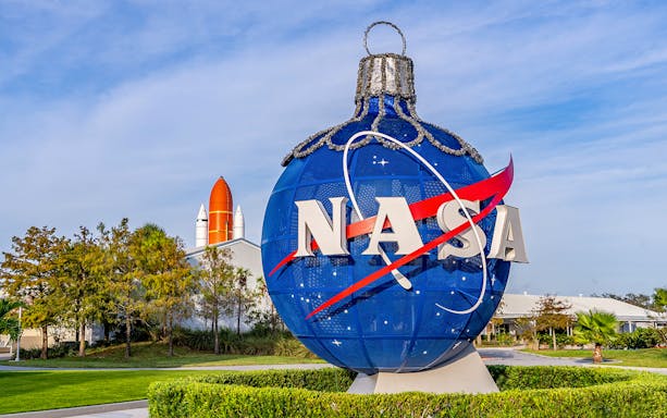 NASA globe sculpture at Kennedy Space Center with space shuttle in background.