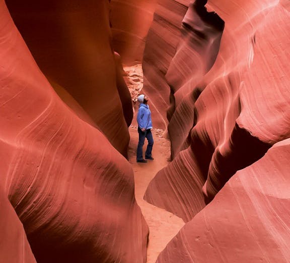 Person exploring narrow passage in Secret Antelope Canyon.