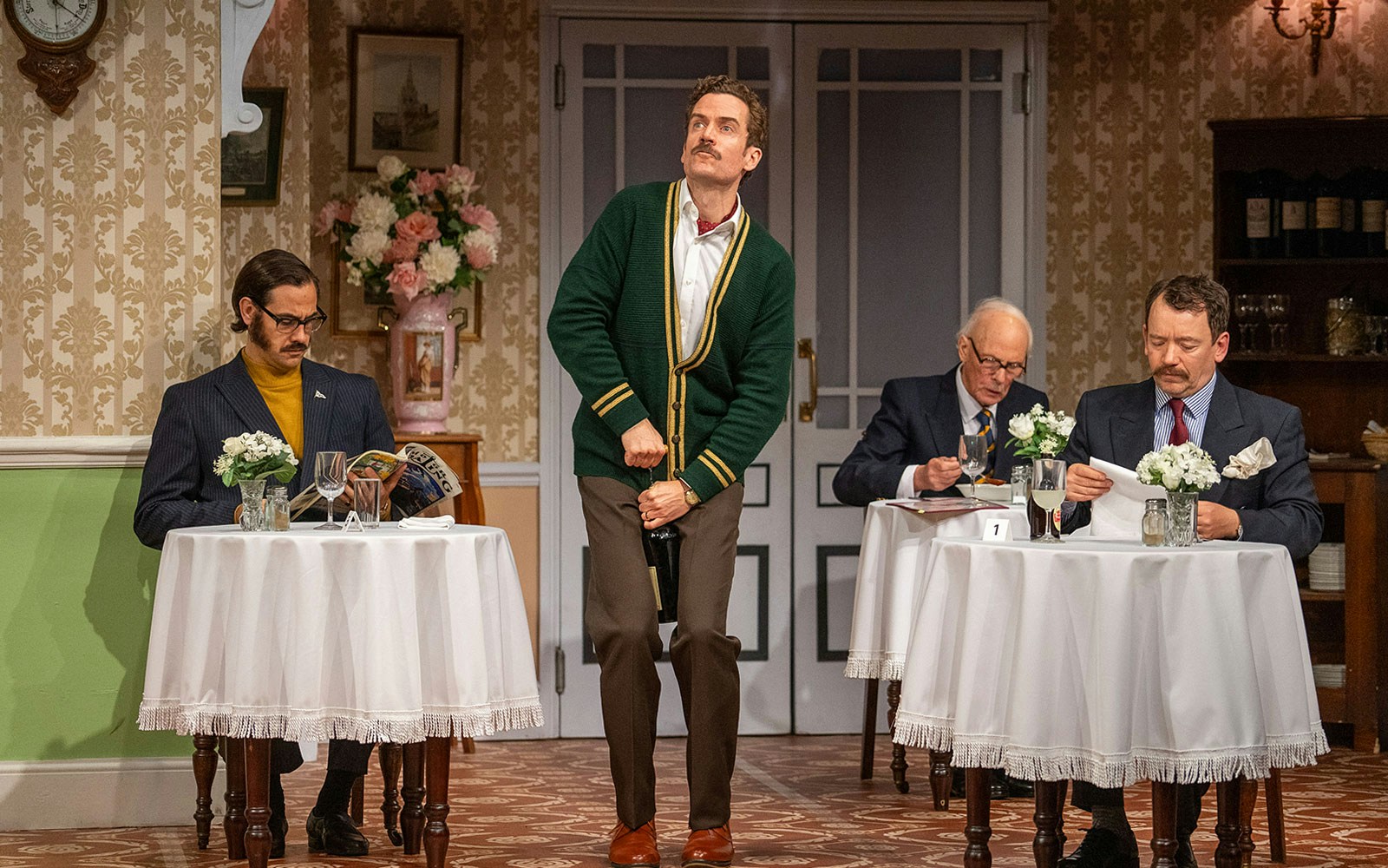 Guests dining at Fawlty Towers-themed restaurant with waiter in green cardigan.