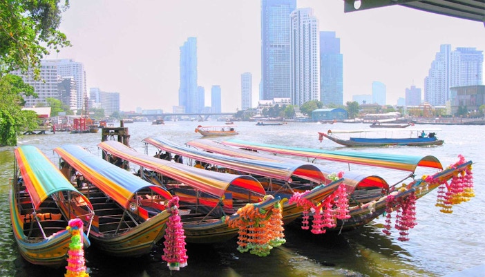 Colorful long-tail boats on a Bangkok canal with city skyline in the background.