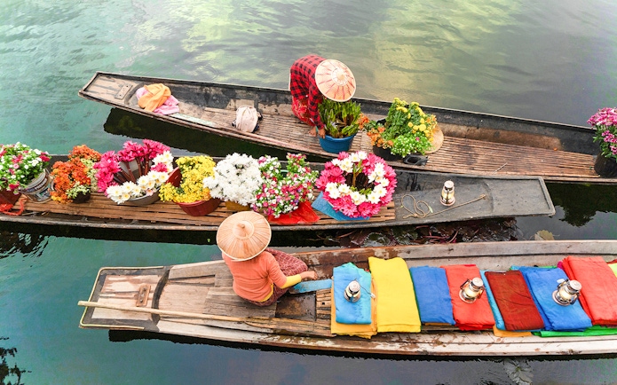Local vendors selling colorful flowers on boats in Amphawa floating market, Thailand.