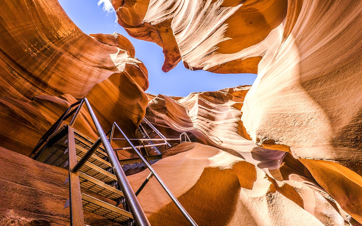 Lower Antelope Canyon ladder entrance with sandstone walls and blue sky.
