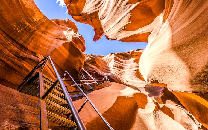 Lower Antelope Canyon ladder entrance with sandstone walls and blue sky.