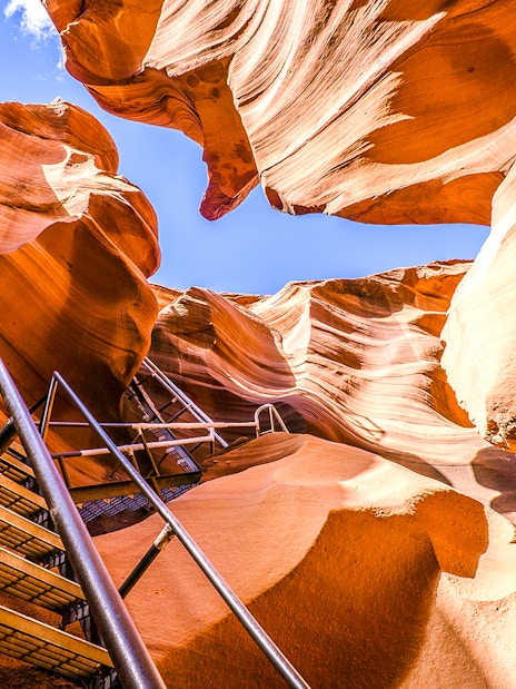 Lower Antelope Canyon ladder entrance with sandstone walls and blue sky.
