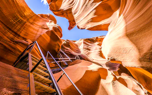 Lower Antelope Canyon ladder entrance with sandstone walls and blue sky.