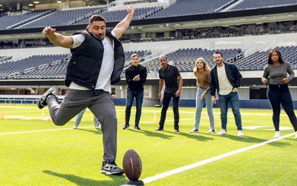 Man kicking football on SoFi Stadium field during tour activity.