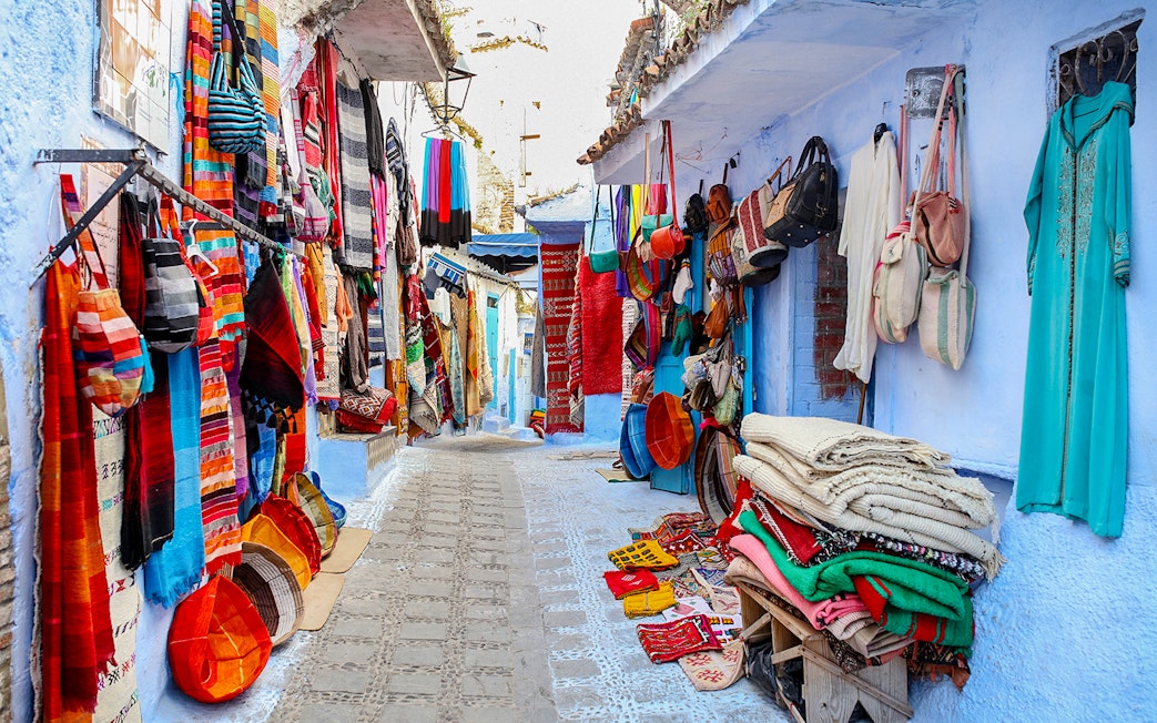 Colorful textiles and bags displayed on a narrow street in Essaouira, Morocco.