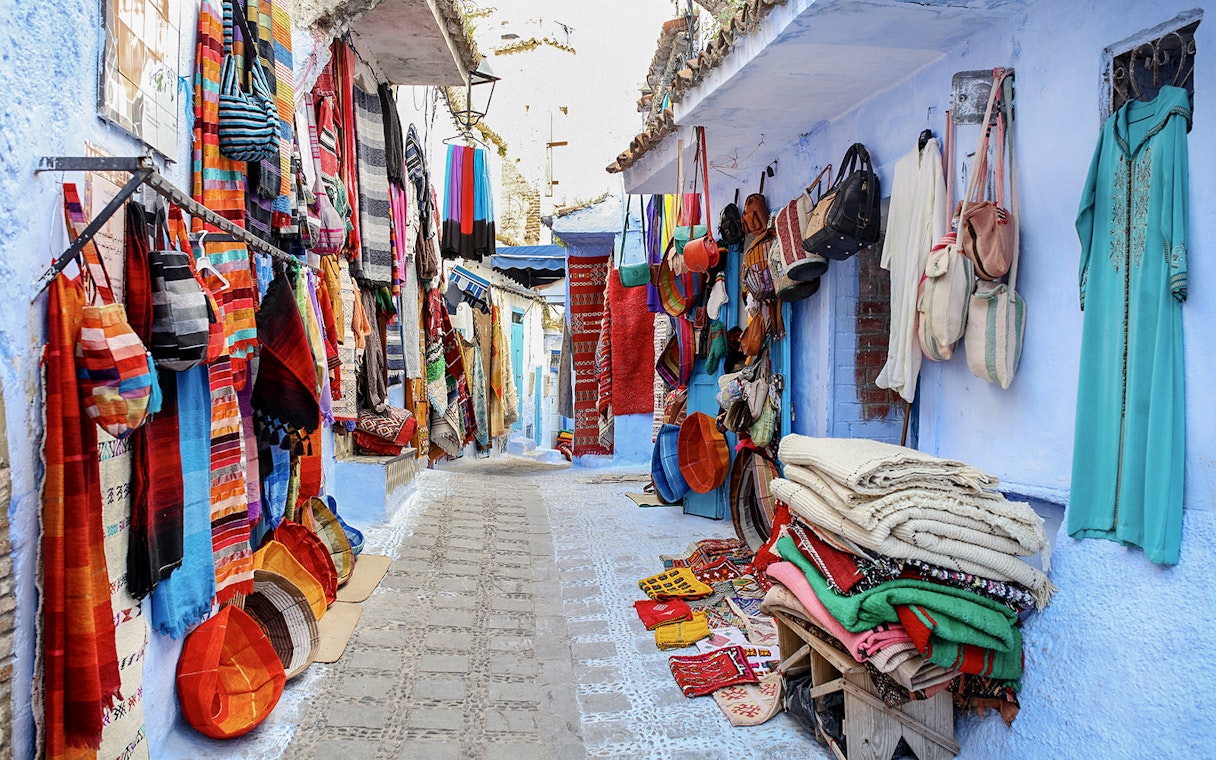 Colorful textiles and bags displayed on a narrow street in Essaouira, Morocco.