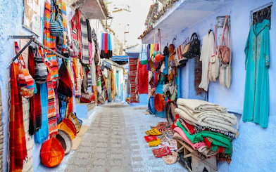 Colorful textiles and bags displayed on a narrow street in Essaouira, Morocco.