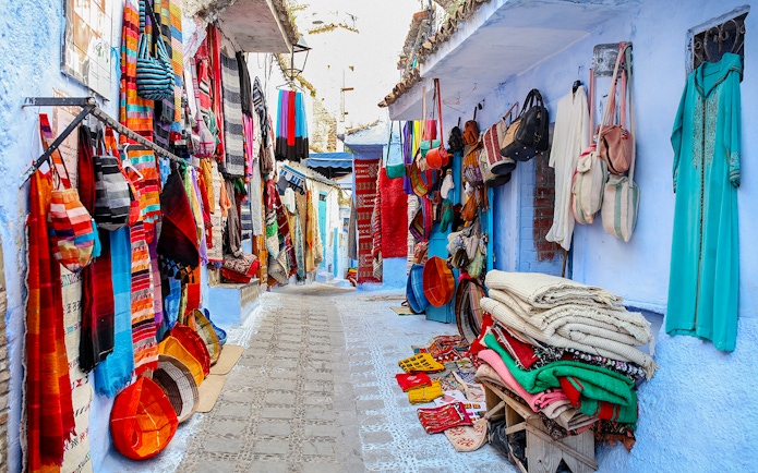 Colorful textiles and bags displayed on a narrow street in Essaouira, Morocco.