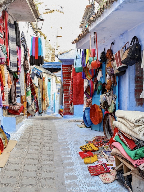 Colorful textiles and bags displayed on a narrow street in Essaouira, Morocco.