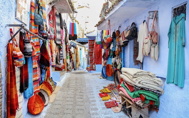 Colorful textiles and bags displayed on a narrow street in Essaouira, Morocco.