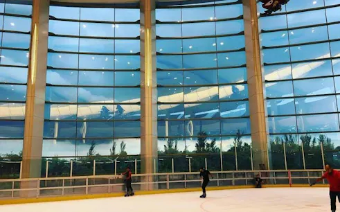 Indoor ice skating rink with skaters, large glass windows, Dubai.
