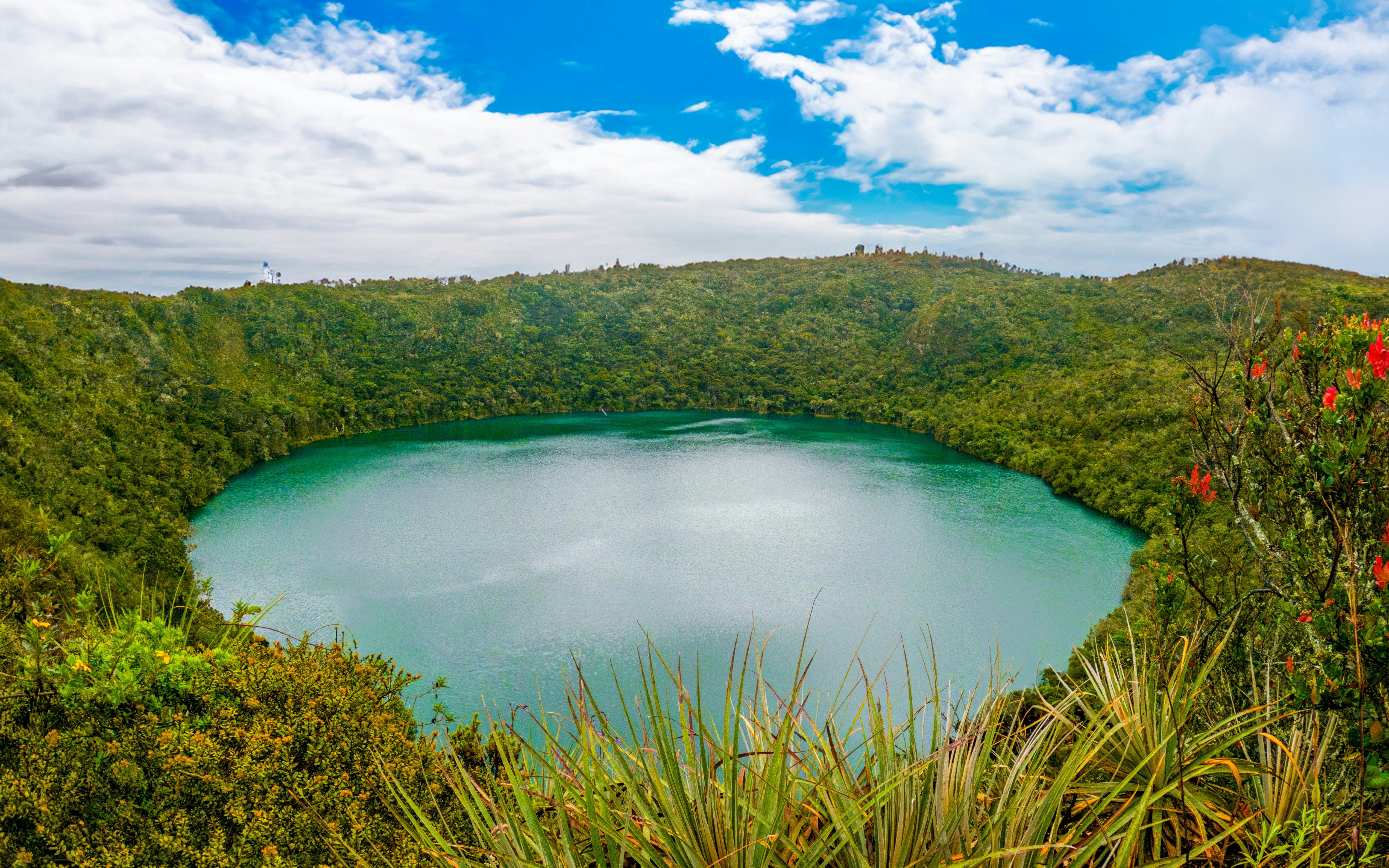 Laguna de Guatavita surrounded by lush greenery under a blue sky in Guatavita, Cundinamarca.