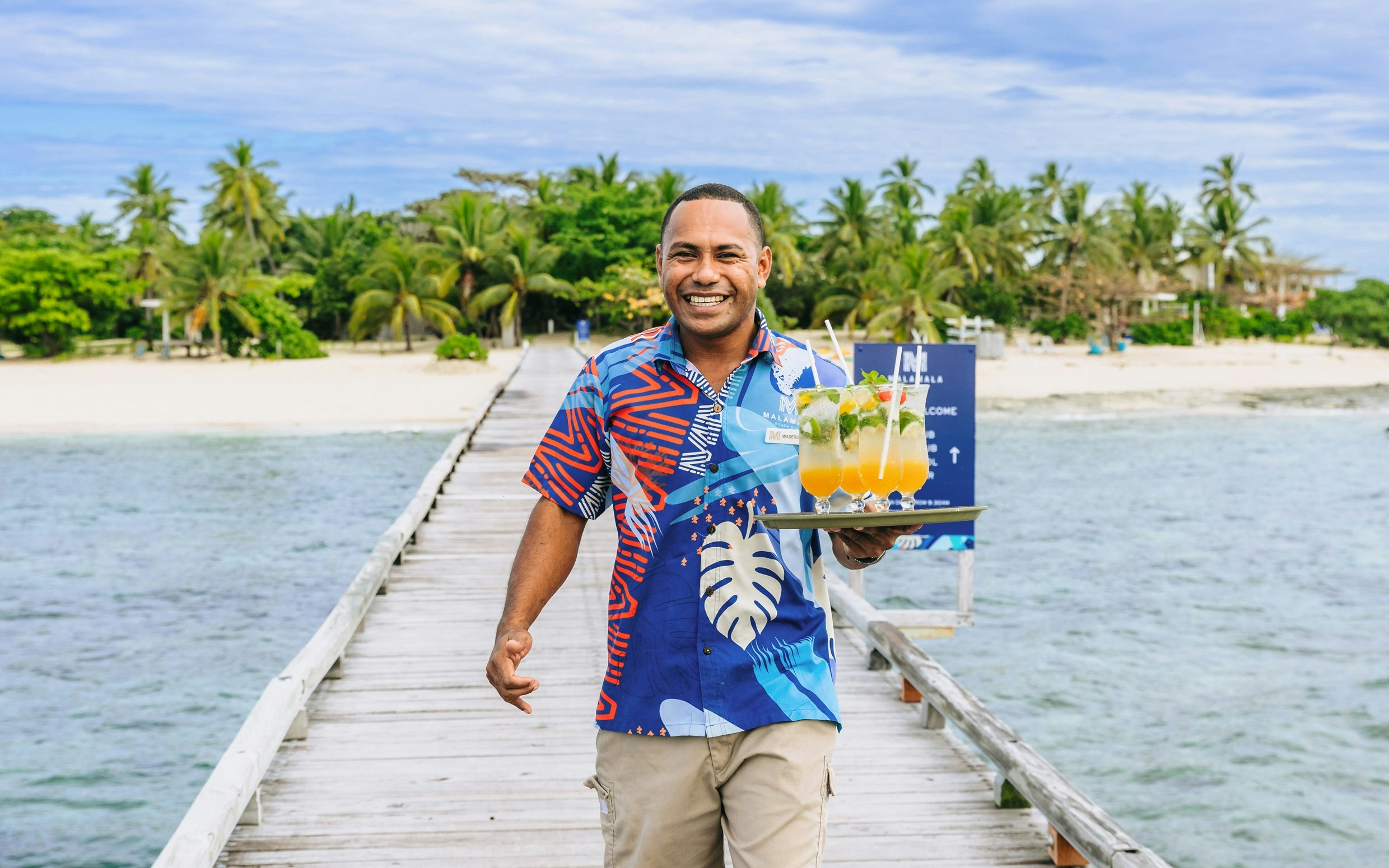 Staff member with drinks on a pier at Malamala Beach Club, Fiji.