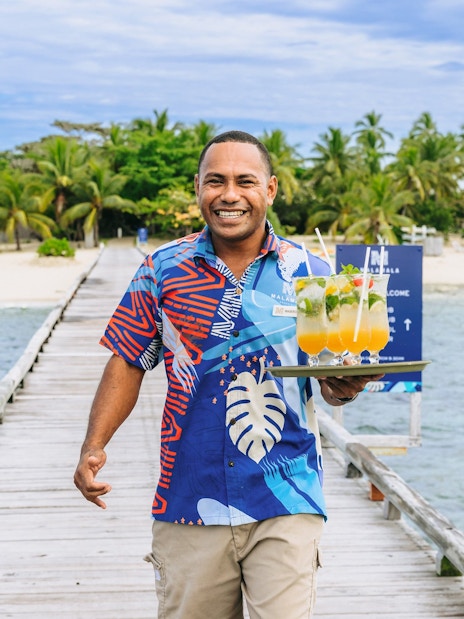 Staff member with drinks on a pier at Malamala Beach Club, Fiji.
