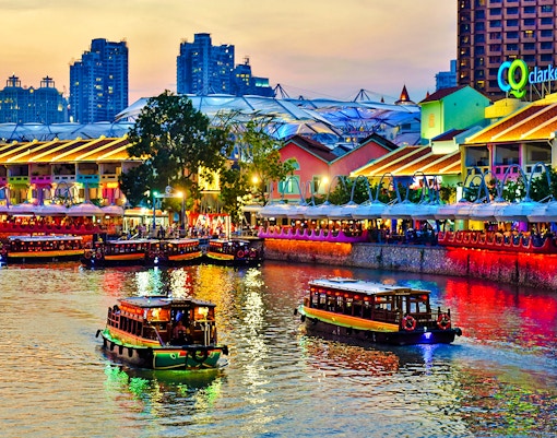 Boats on the Singapore River at Clarke Quay, illuminated buildings and vibrant nightlife.