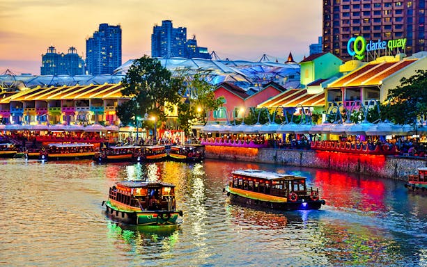 Boats on the Singapore River at Clarke Quay, illuminated buildings and vibrant nightlife.