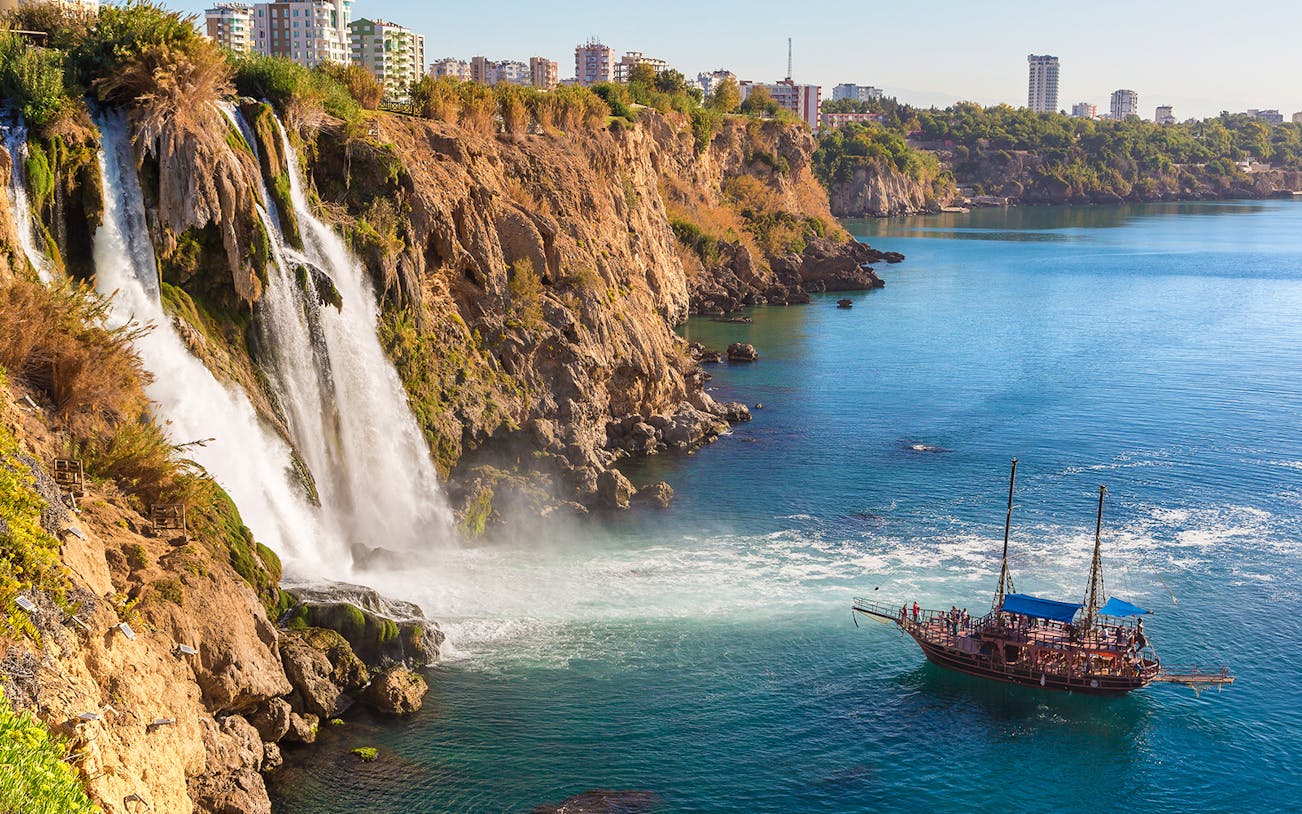 Waterfall cascading into the sea with a boat nearby in Antalya, Turkey.