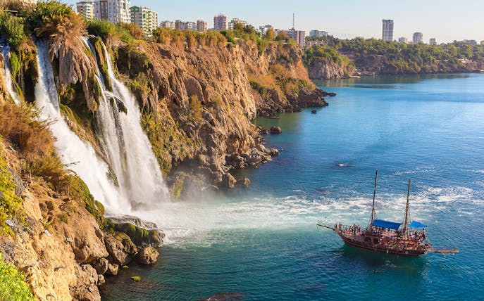 Waterfall cascading into the sea with a boat nearby in Antalya, Turkey.